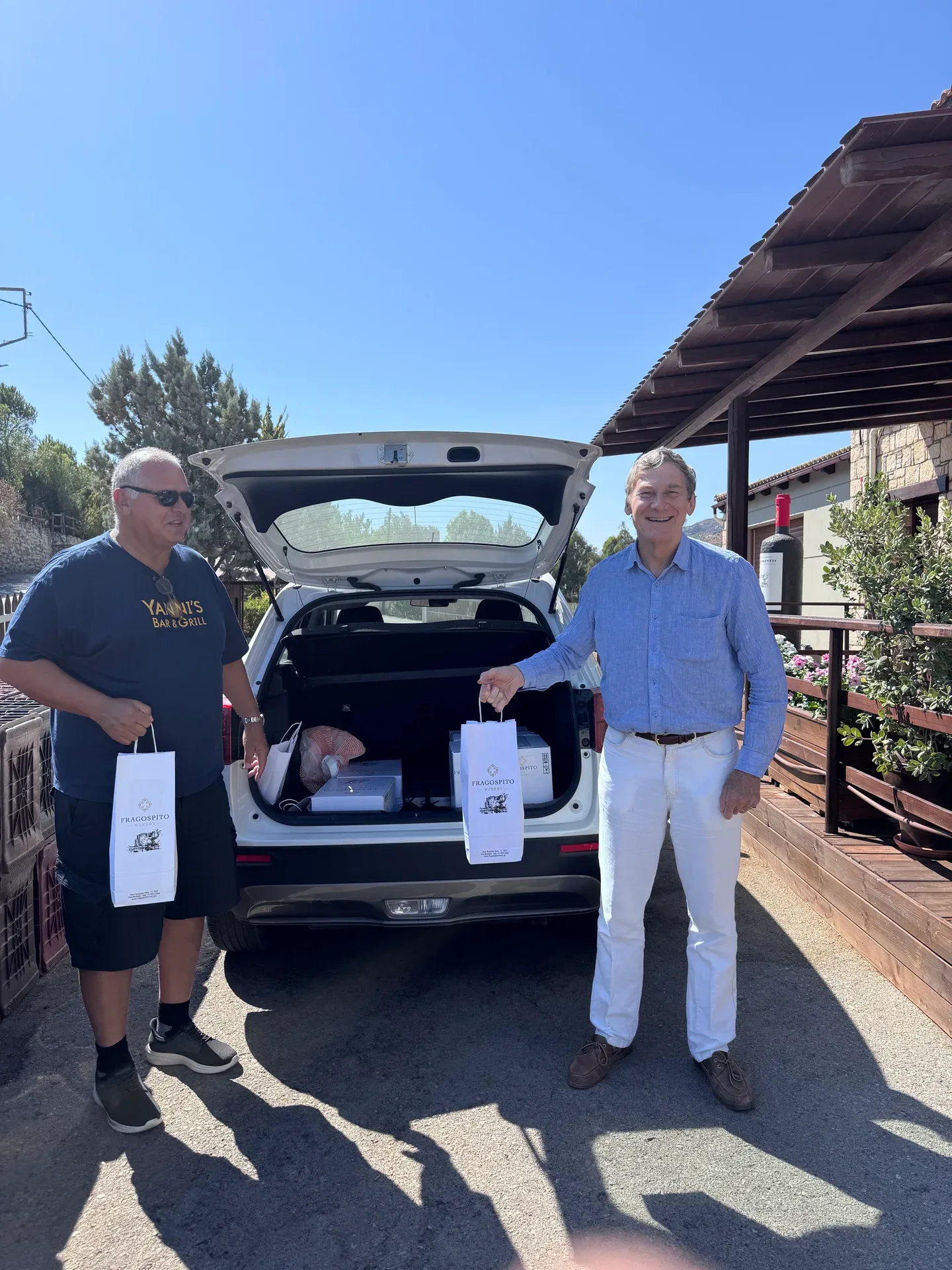 Visitors with wine bags beside a car trunk filled with wine boxes