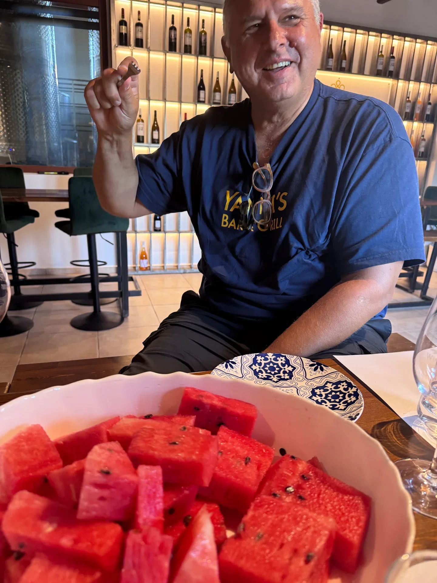 A smiling guest with a glass of wine behind a bowl of watermelon