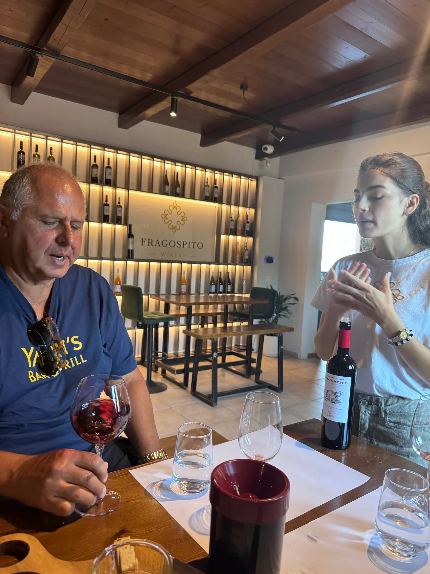 Yanni tasting red wine with a winery host at the table