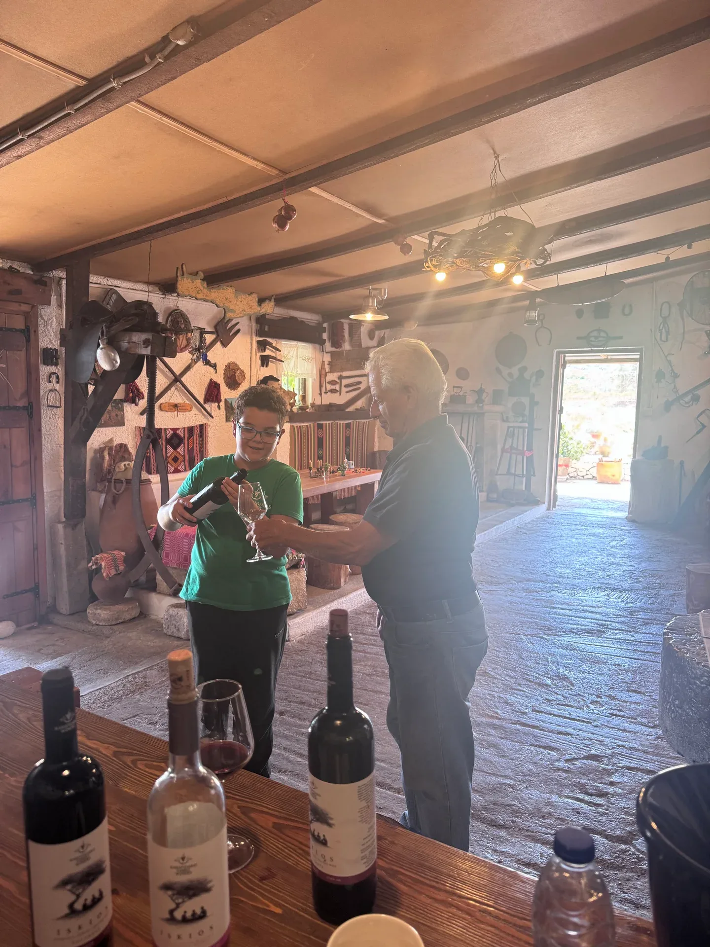 A young host pouring wine for an older family member, with bottles on the table