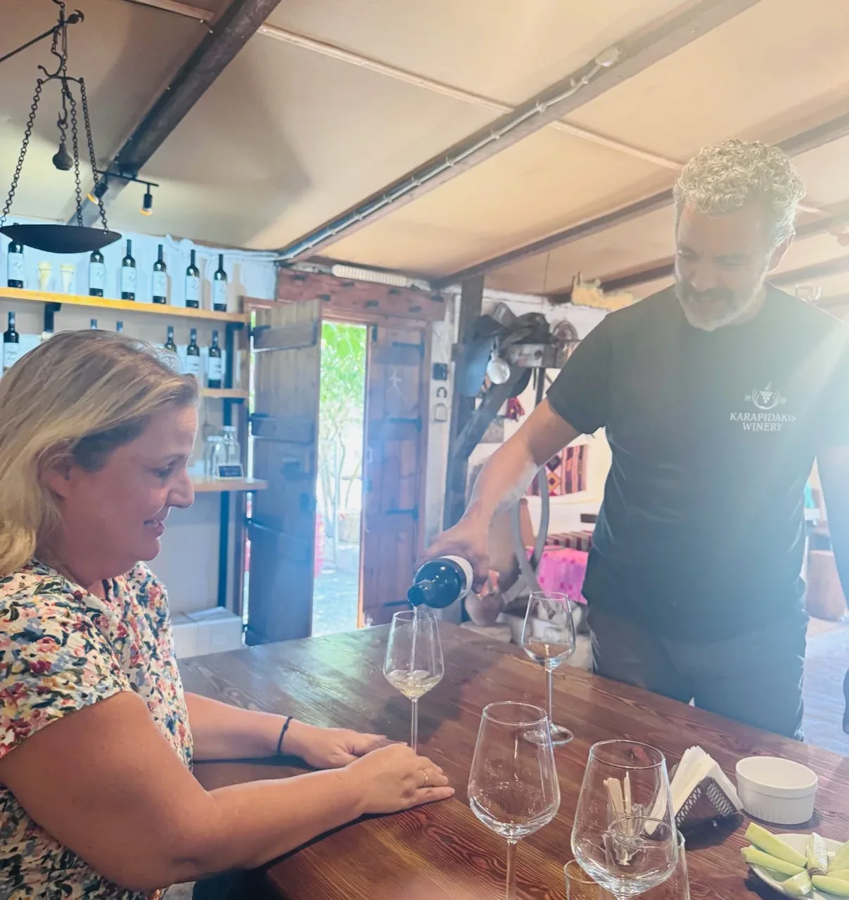A Karapidakis host pouring white wine for a guest at the tasting table