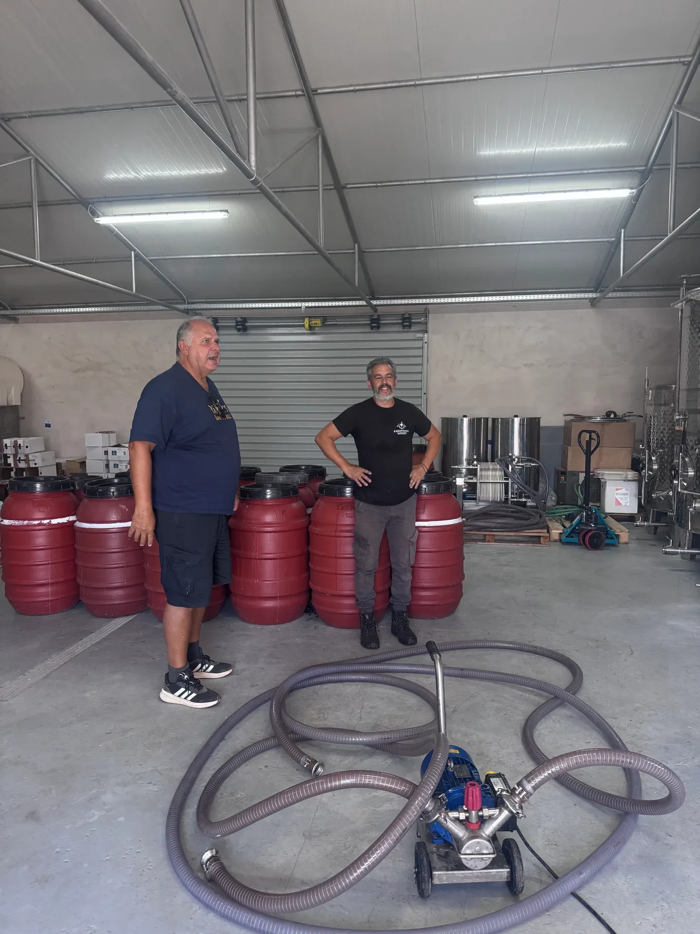 Yanni and a Karapidakis host standing among tanks and barrels in the production room