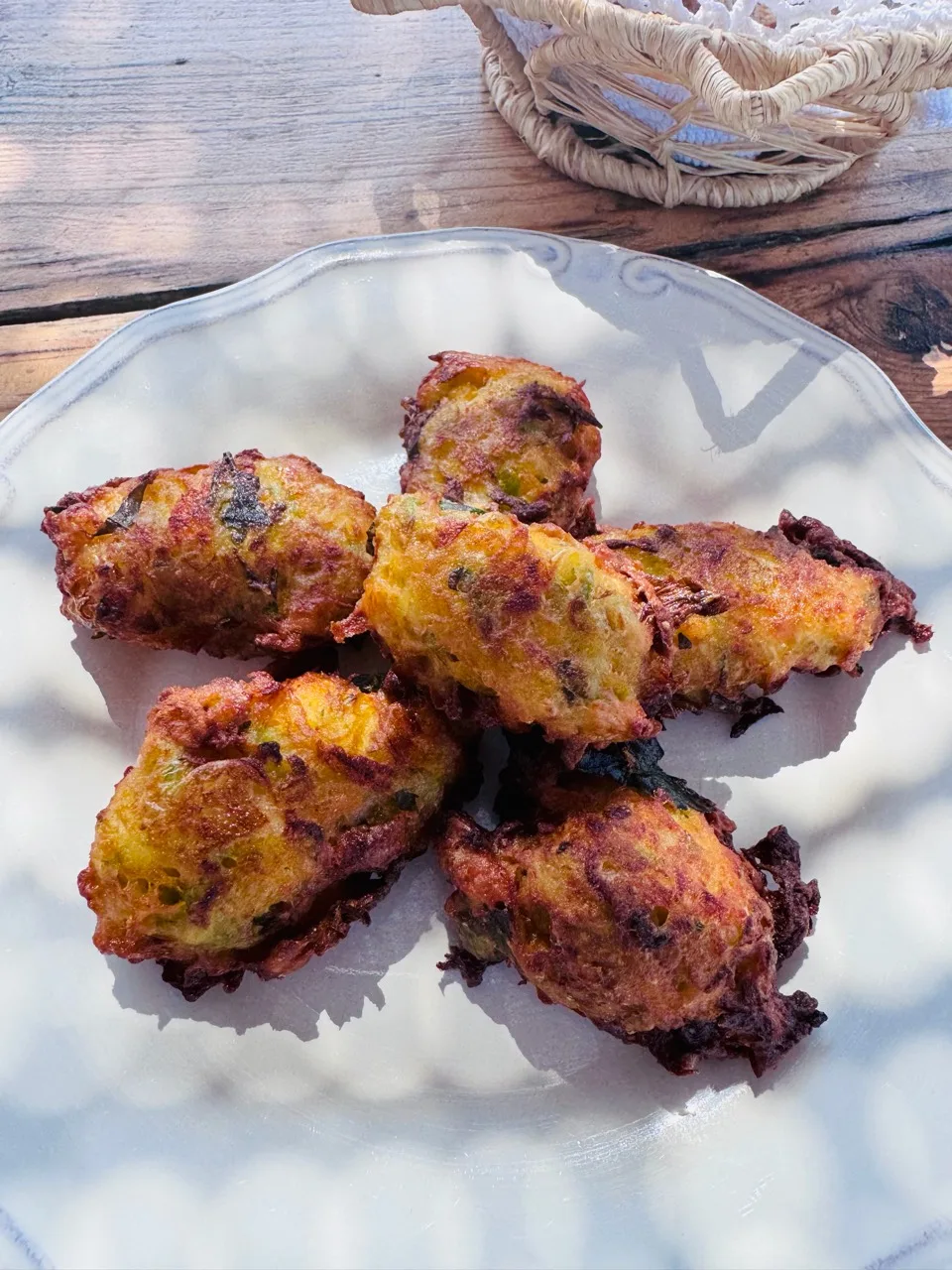 Golden zucchini fritters piled on a white plate on the outdoor wooden table