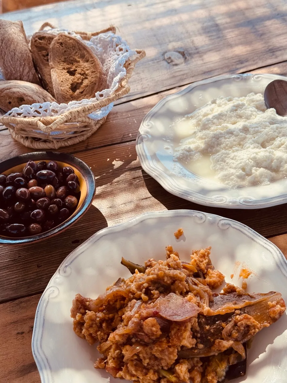 Plates of fresh white cheese and eggplant with bulgur beside olives and a basket of bread