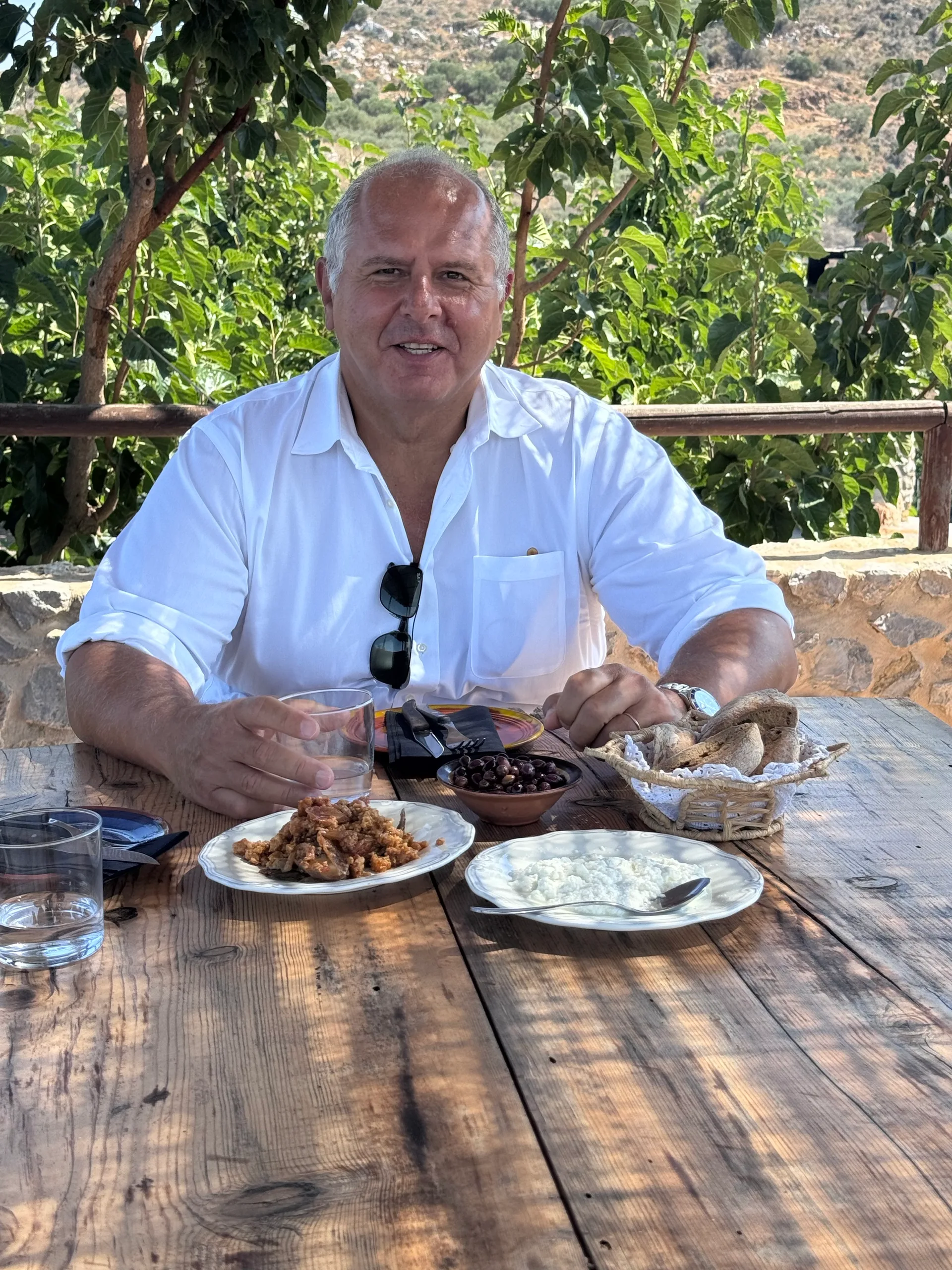A closer portrait of a man in a white shirt at the shaded table, with the lunch dishes in front