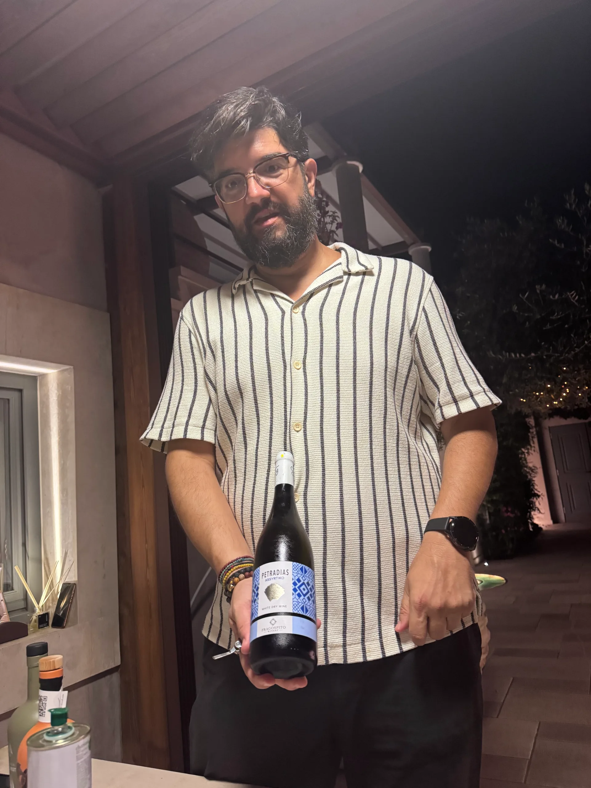 A man in glasses presenting a bottle labeled Petradias Assyrtiko, Fragospito