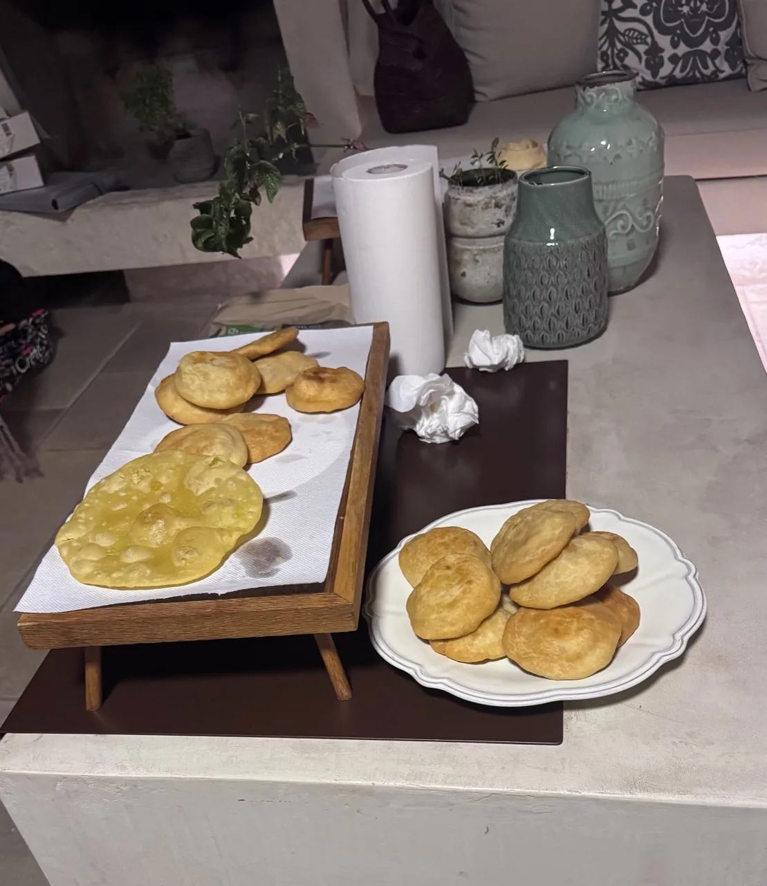 Golden round pastries on a raised wooden tray and a white plate beside the preparation table