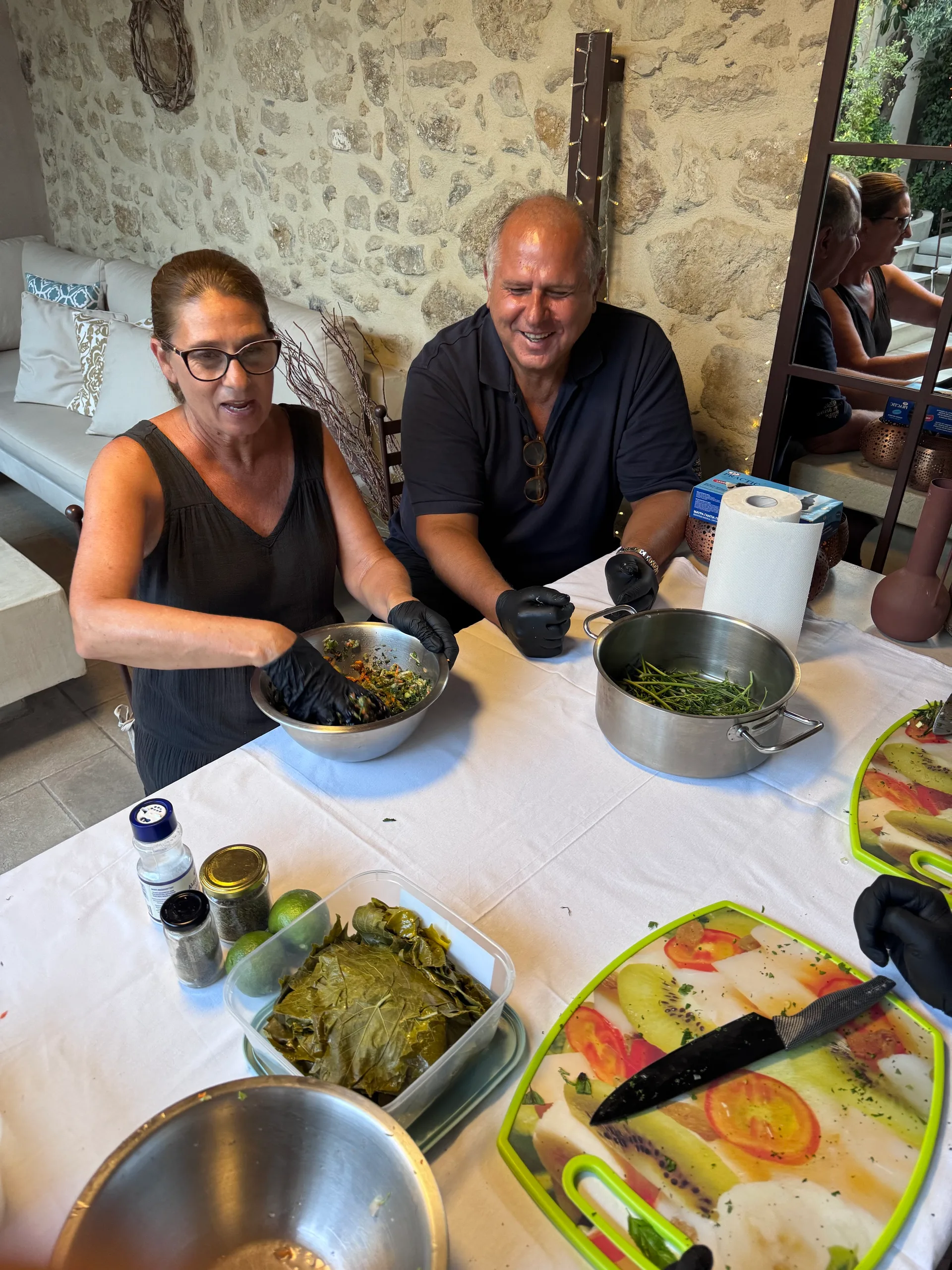 Two participants laughing at the cooking table with a bowl of filling and grape leaves in front of them