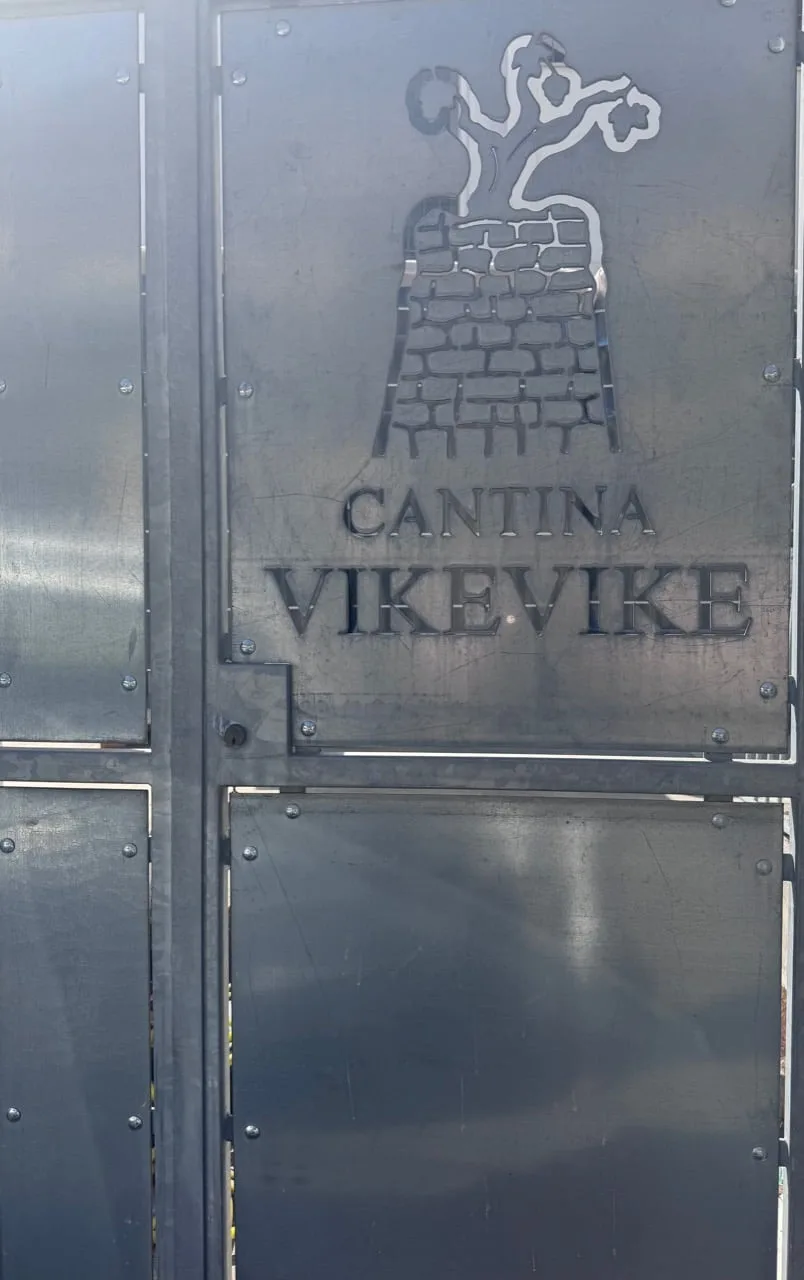 Metal gate bearing the Cantina Vike Vike name and tree-topped stone tower mark